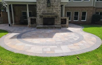 A spacious, modern terrace with stone flooring and an outdoor fireplace, surrounded by a well-maintained green lawn, an example of aesthetic landscape design by Everlast Lawns and Landscapes.