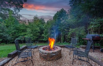 Roaring fire in a stone firepit with wood logs and surrounded by trees at dusk in a backyard