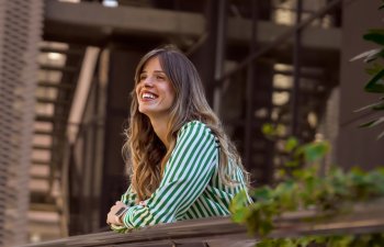 Smiling Woman Leaning on Railing in Green Striped Shirt Outdoors contemplating. Portrait of a confident young businesswoman in front of the modern office building.
