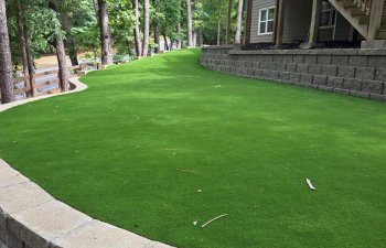 Backyard artificial grass installation with stone retaining wall and wooden deck